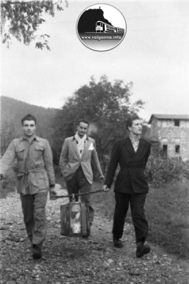 6 Movimento Resistenza Partigiana. Due partigiani camminano per una strada di campagna trasportando una valigia appesa ad un bastone - un altro uomo li segue..jpg
