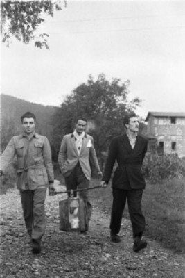 Movimento Resistenza Partigiana. Due partigiani camminano per una strada di campagna trasportando una valigia appesa ad un bastone - un altro uomo li segue..jpg